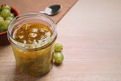 Photo of Jar of delicious gooseberry jam and fresh berries on wooden table, closeup. Space for text