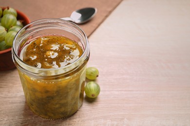 Jar of delicious gooseberry jam and fresh berries on wooden table, closeup. Space for text