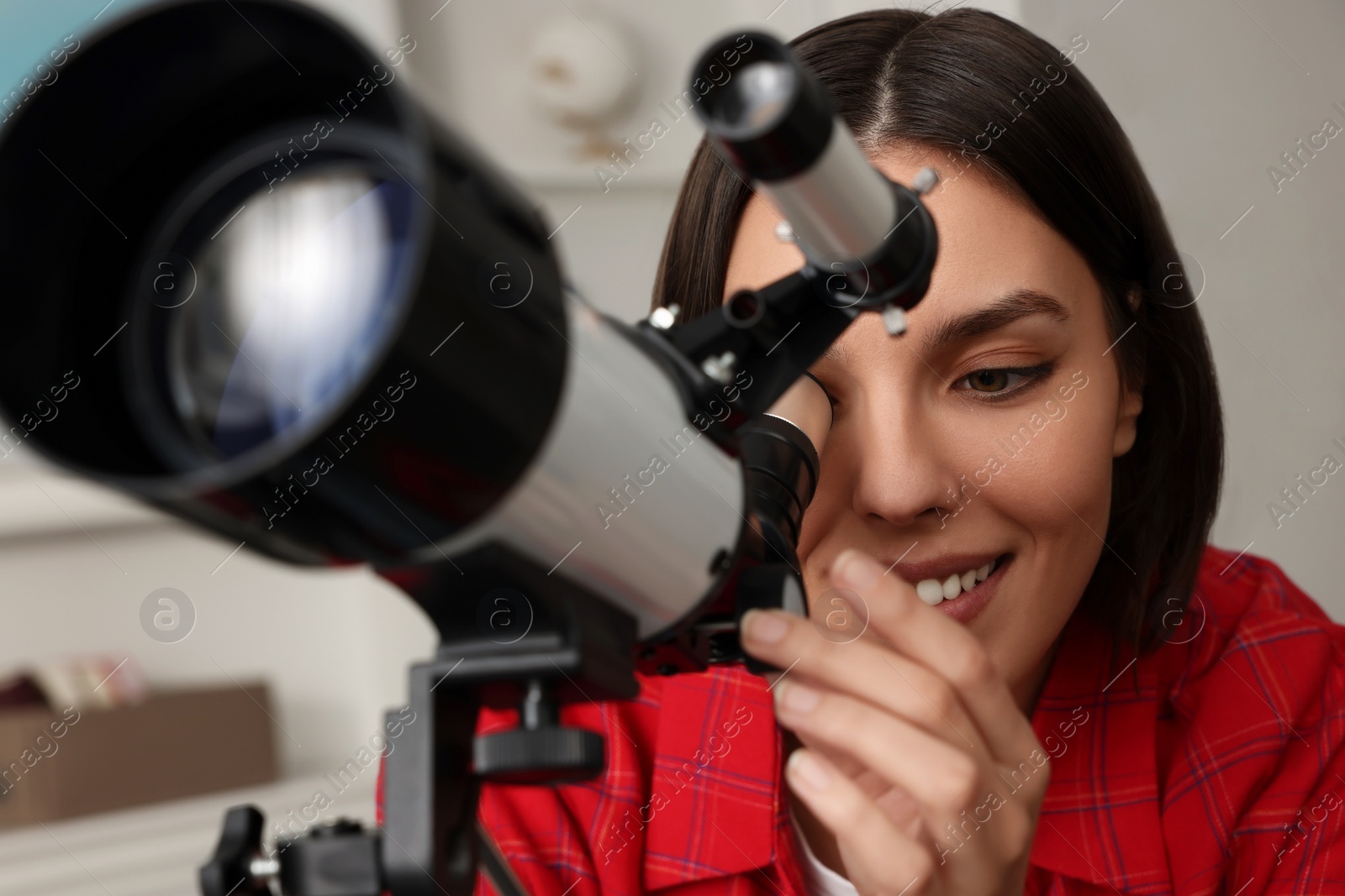 Photo of Beautiful young woman looking at stars through telescope in room, closeup