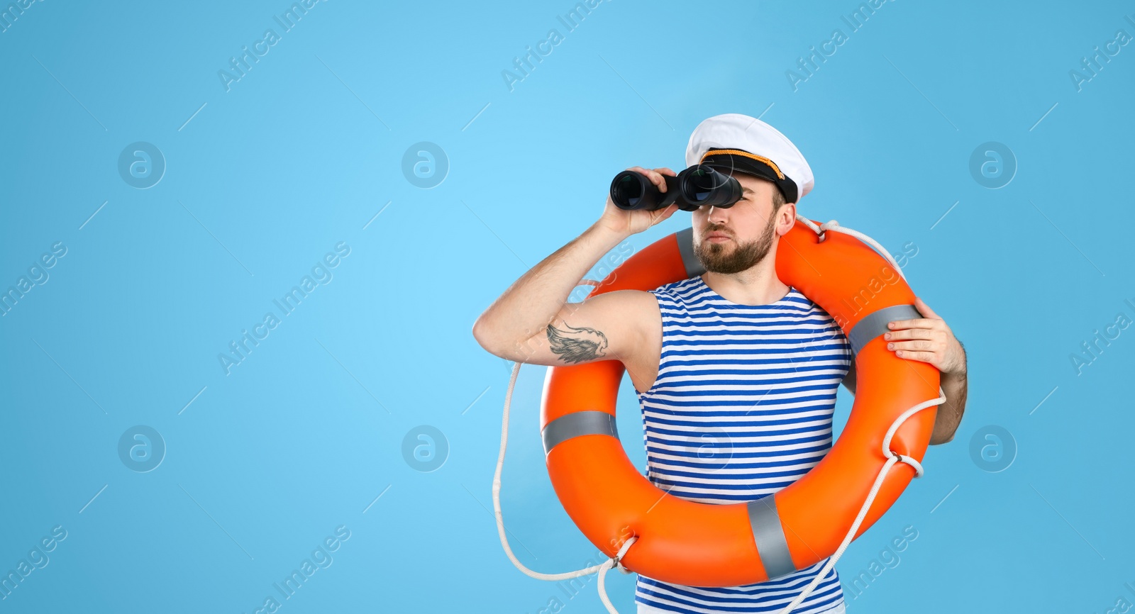 Photo of Sailor with binoculars and ring buoy on light blue background