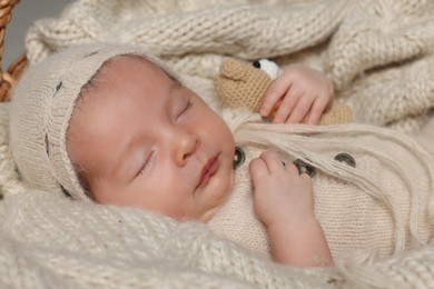 Adorable newborn baby with toy bear sleeping on knitted plaid, closeup