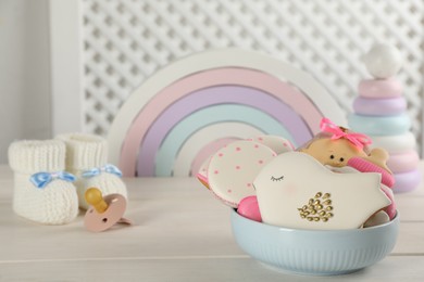 Cute tasty cookies of different shapes, toys and accessories on white wooden table, space for text. Baby shower party