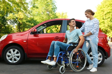 Photo of Young woman with disabled man in wheelchair near car outdoors
