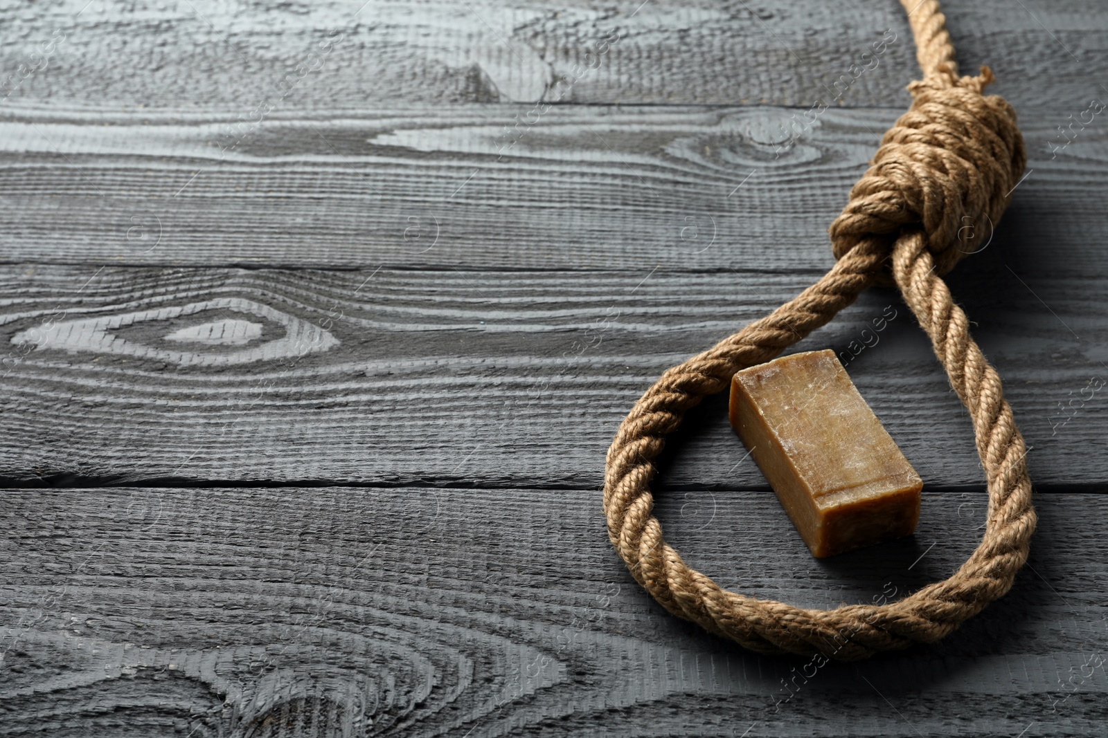 Photo of Rope noose and soap bar on grey wooden table. Space for text