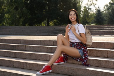 Photo of Beautiful young woman with stylish beige backpack on stairs outdoors, space for text