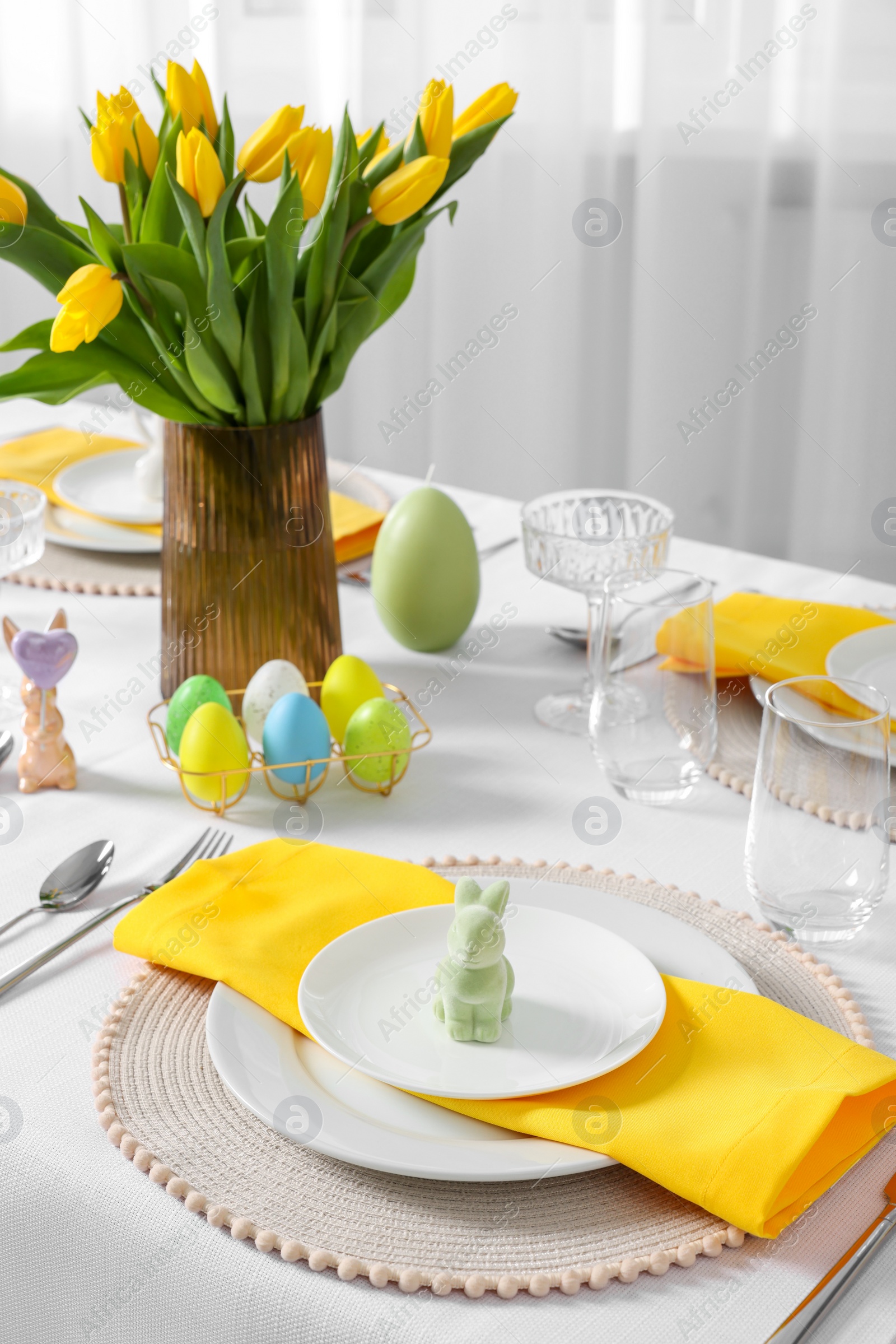 Photo of Festive table setting with glasses, painted eggs and vase of tulips. Easter celebration