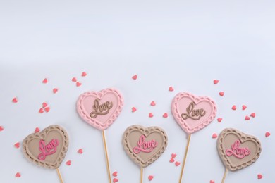 Photo of Different chocolate heart shaped lollipops and sprinkles on white background, flat lay. Space for text