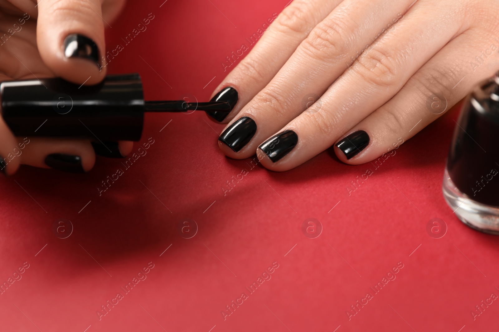 Photo of Woman applying black nail polish on color background, closeup