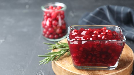 Photo of Fresh cranberry sauce and rosemary in glass bowl on gray table, closeup. Space for text