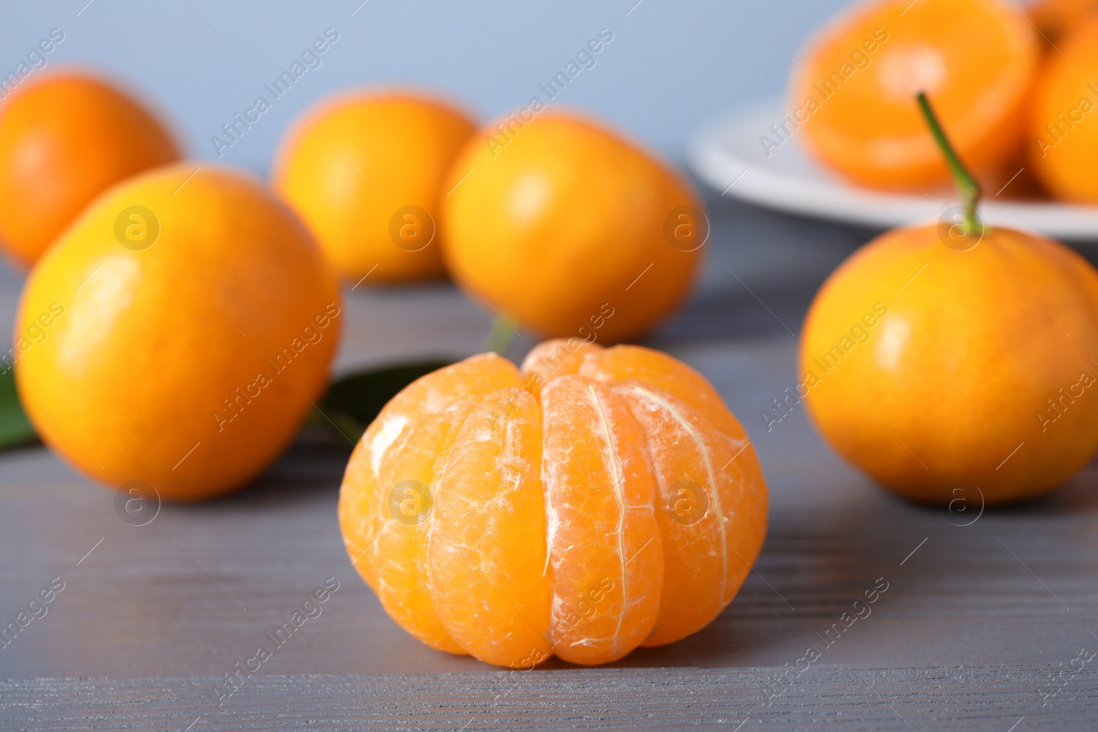 Photo of Peeled fresh ripe tangerine on grey wooden table, closeup