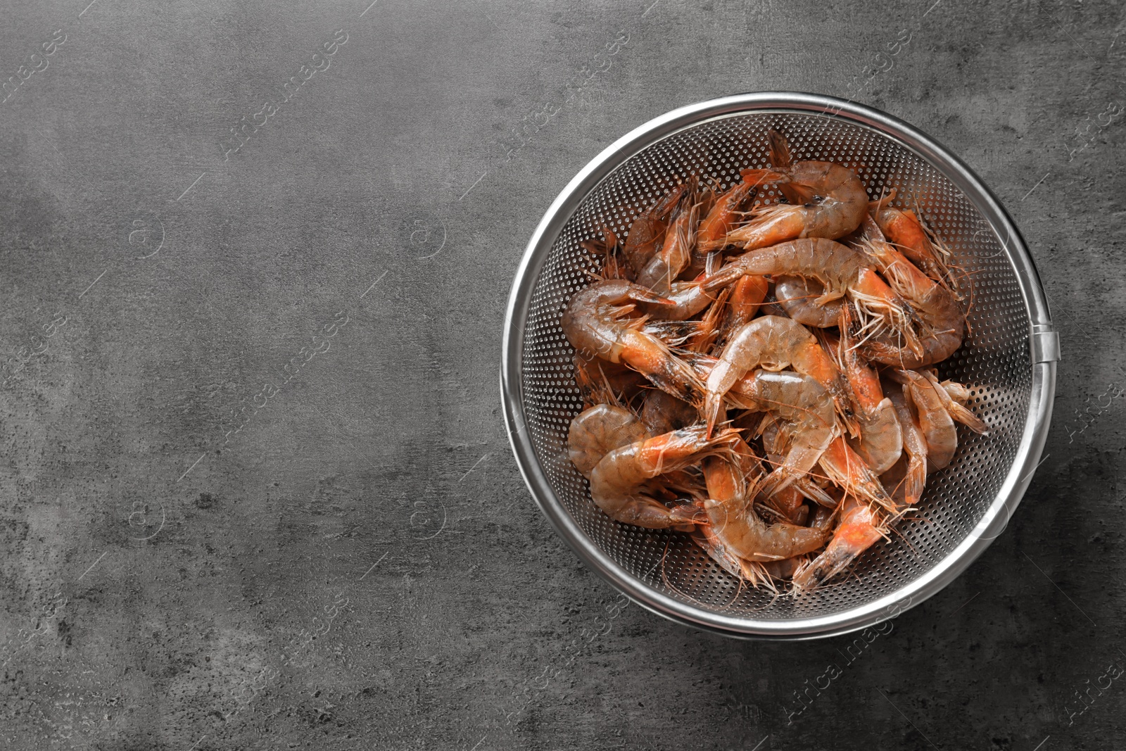 Photo of Colander with fresh shrimps on gray background