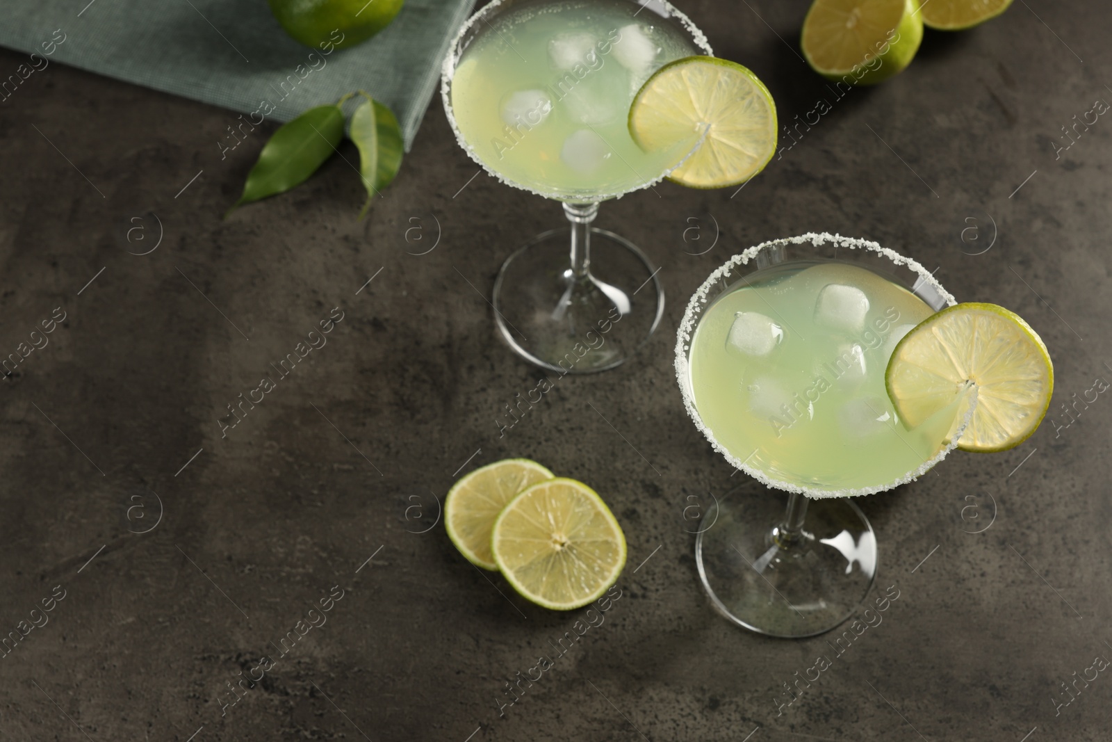 Photo of Delicious Margarita cocktail with ice cubes in glasses and limes on grey table, space for text