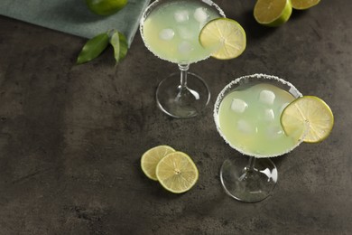 Delicious Margarita cocktail with ice cubes in glasses and limes on grey table, space for text