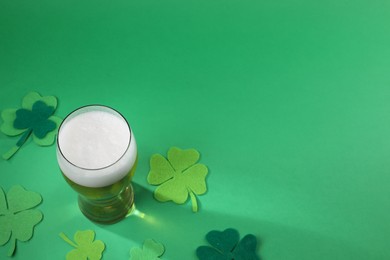 Photo of St. Patrick's day party. Green beer in glass and decorative clover leaves on green background, above view. Space for text