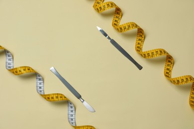 Photo of Scalpels and measuring tape on beige background, flat lay with space for text. Weight loss surgery