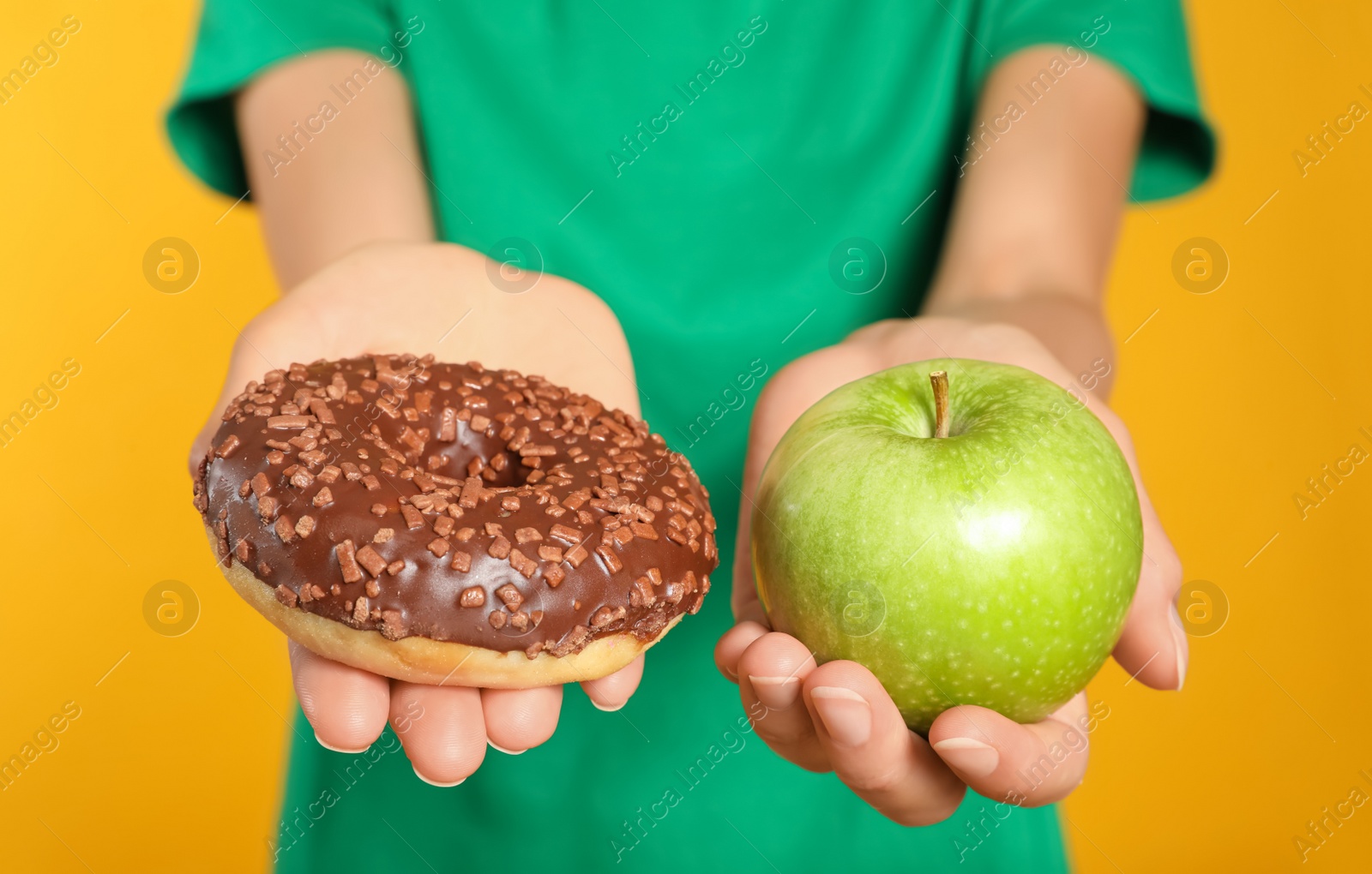 Photo of Woman choosing between doughnut and healthy apple on yellow background, closeup