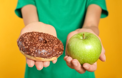 Photo of Woman choosing between doughnut and healthy apple on yellow background, closeup