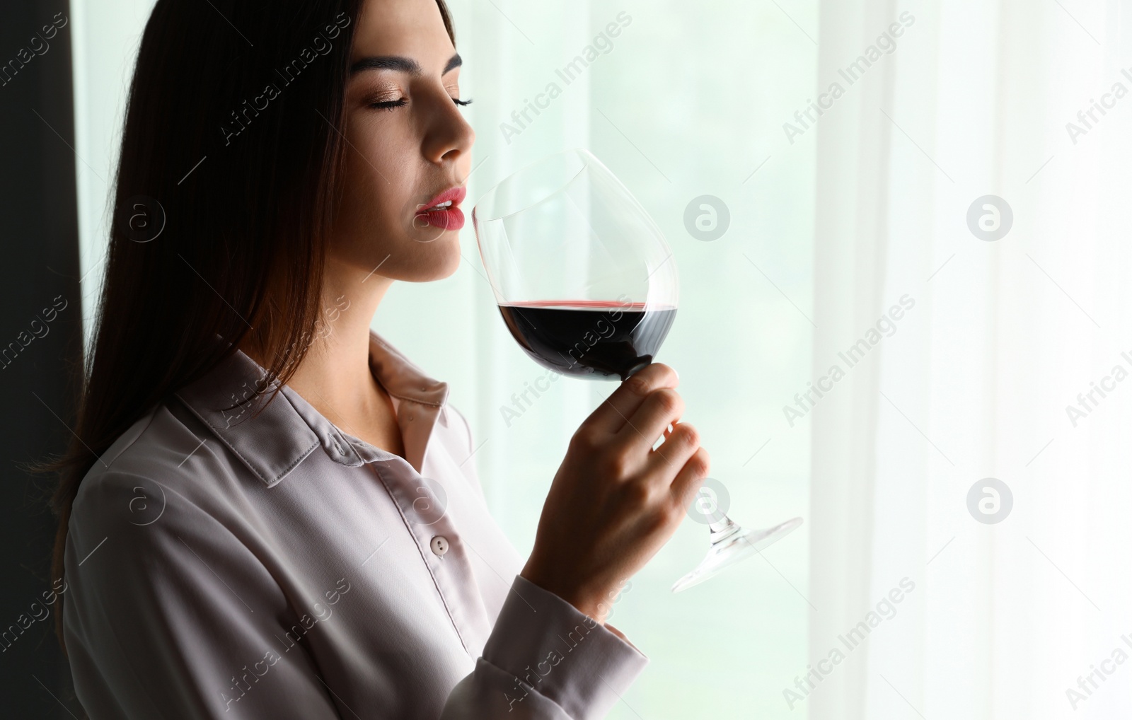 Photo of Beautiful young woman with glass of luxury red wine indoors. Space for text