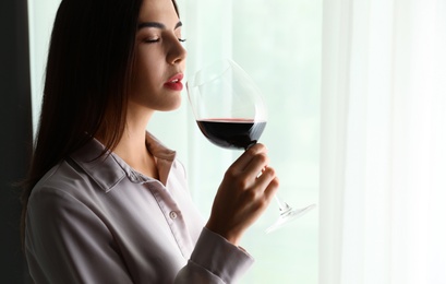 Photo of Beautiful young woman with glass of luxury red wine indoors. Space for text