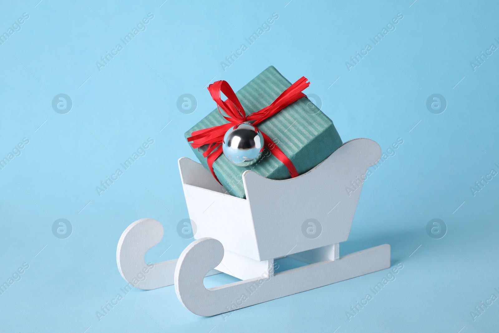 Photo of White wooden sleigh with gift box and Christmas ball on light blue background