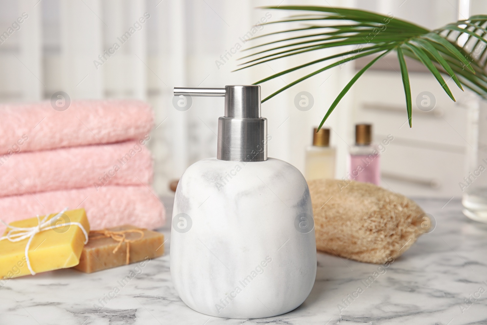 Photo of Marble dispenser, soap bars and luffa sponge on table