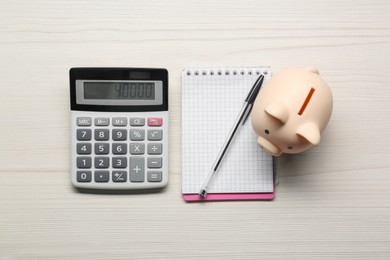 Calculator, piggy bank, notebook and pen on white wooden table, flat lay