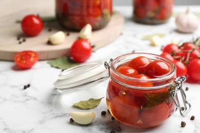 Photo of Glass jar of pickled cherry tomatoes and ingredients on white marble table. Space for text