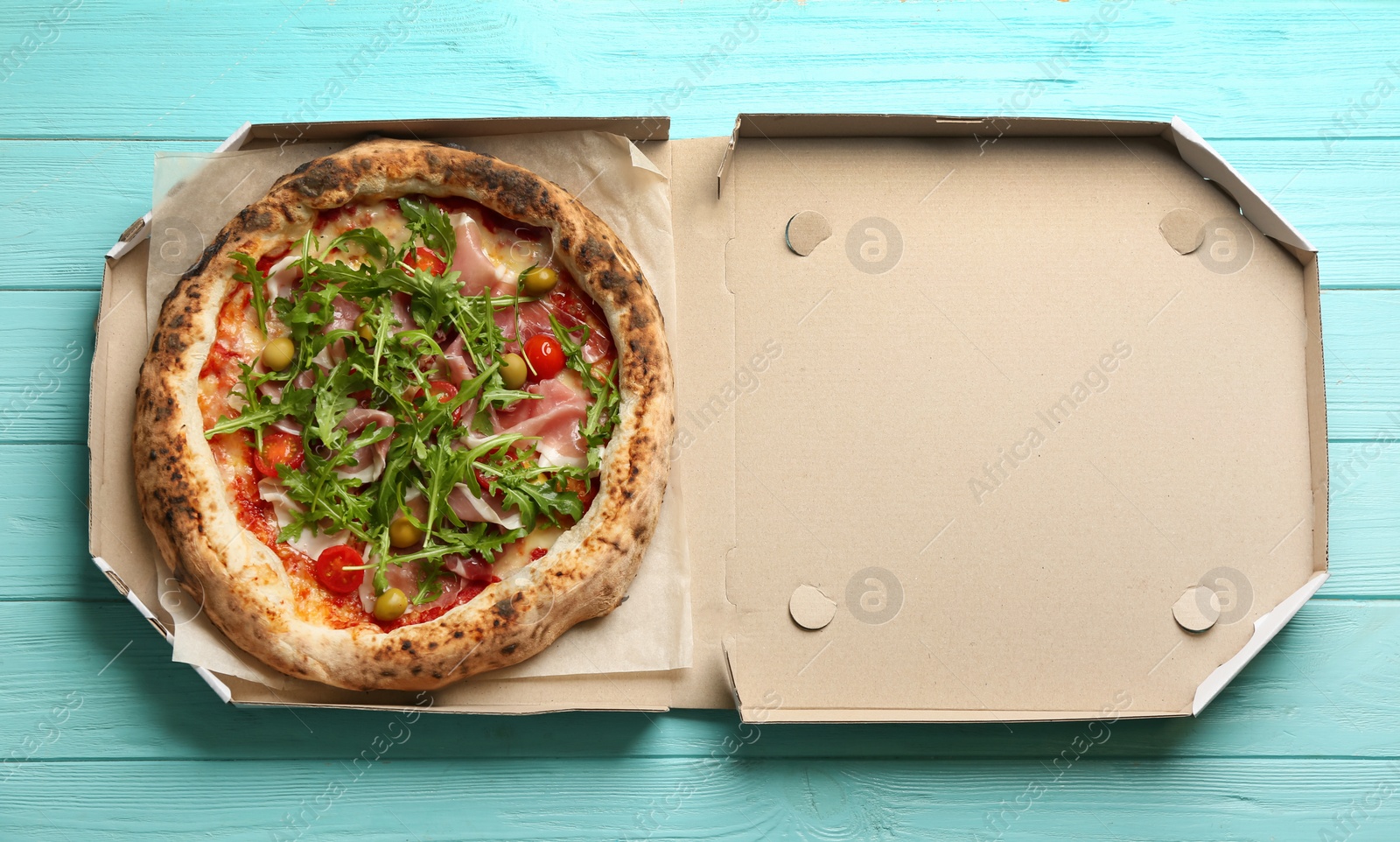 Photo of Tasty pizza with meat and arugula in cardboard box on light blue wooden table, top view