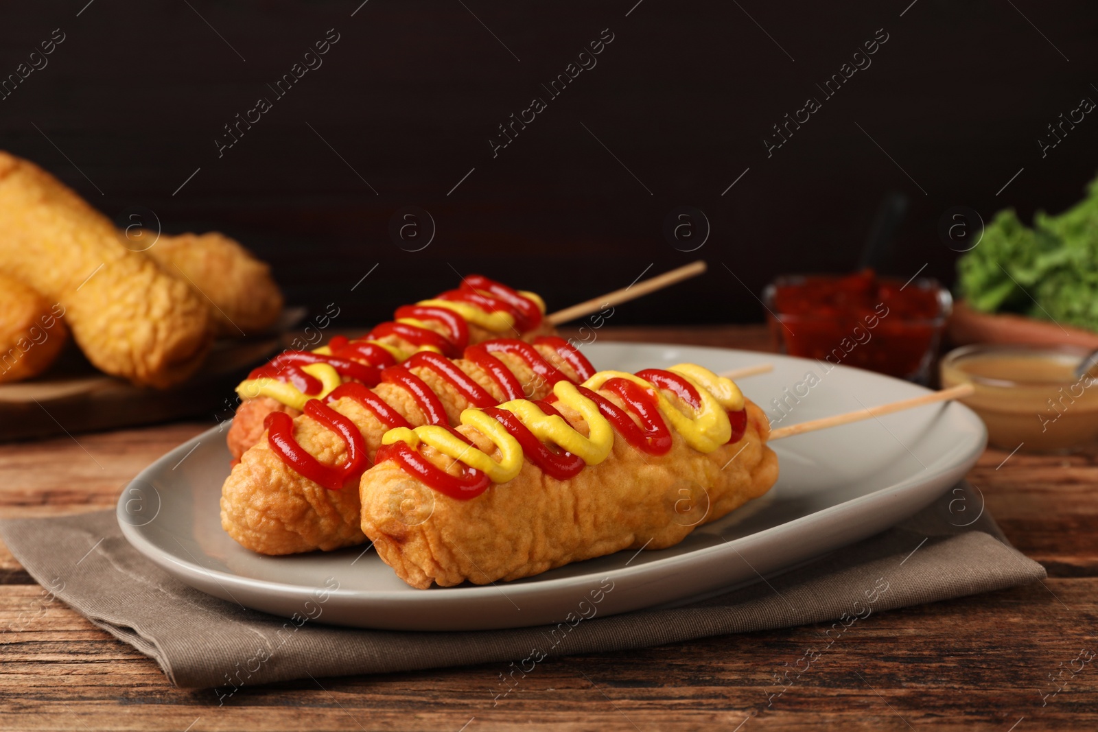 Photo of Delicious corn dogs with mustard and ketchup on wooden table