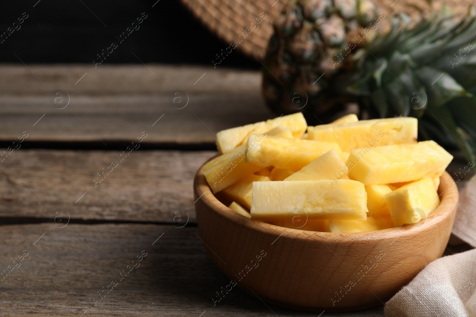 Photo of Pieces of tasty ripe pineapple in bowl on wooden table. Space for text