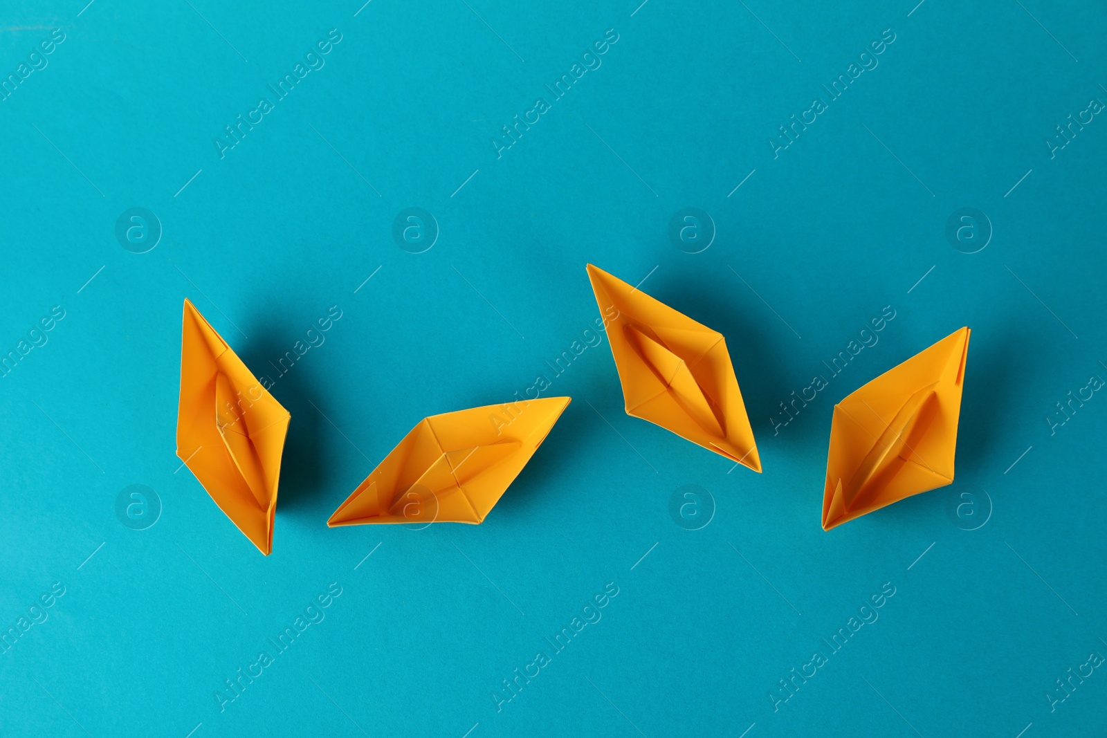 Photo of Handmade orange paper boats on light blue background, flat lay. Origami art