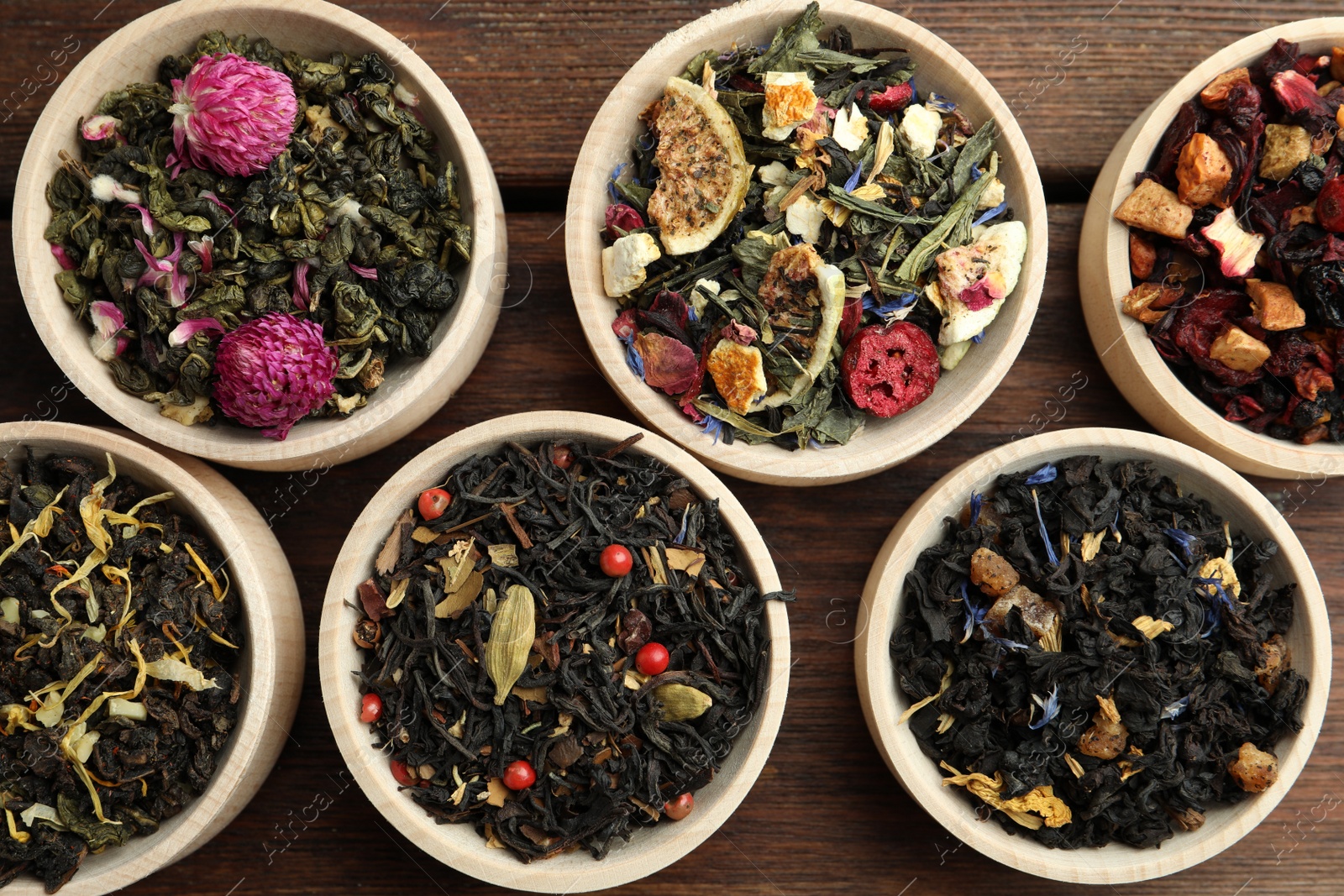 Photo of Different kinds of dry herbal tea in bowls on wooden table, flat lay