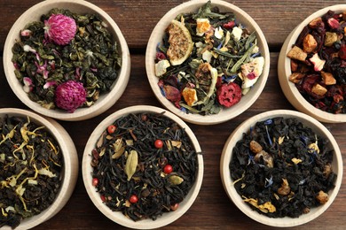Different kinds of dry herbal tea in bowls on wooden table, flat lay