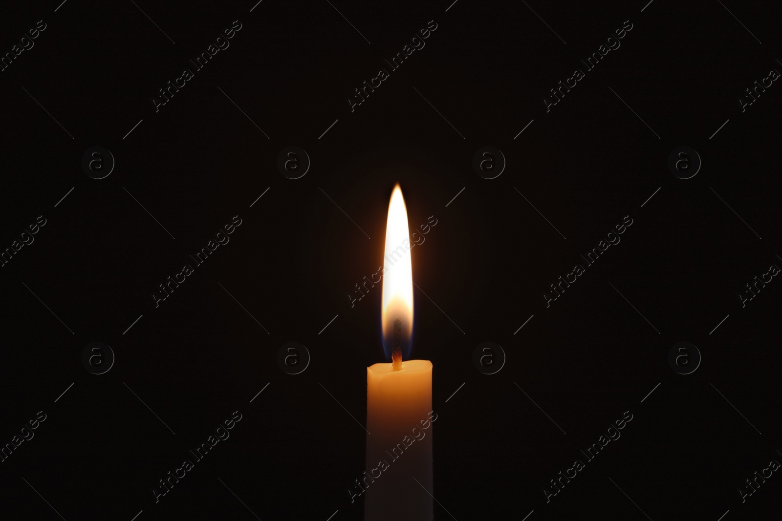 Photo of Wax candle burning on black background, closeup