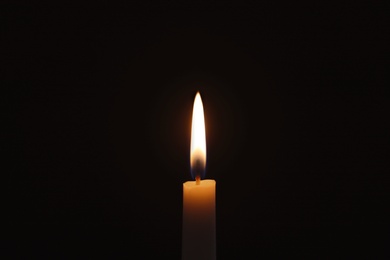 Photo of Wax candle burning on black background, closeup