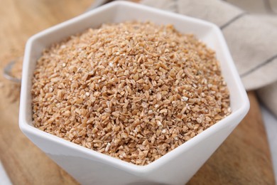 Dry wheat groats in bowl on table, closeup