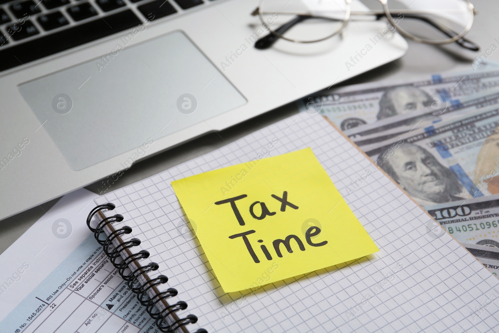 Photo of Reminder note with words Tax Time, documents and money near laptop on grey table, closeup