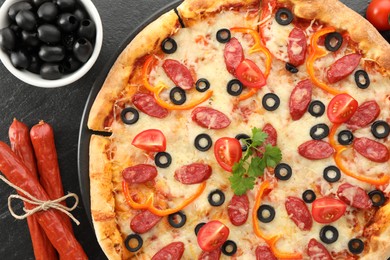 Photo of Tasty pizza with dry smoked sausages, olives, tomato, pepper and parsley on grey table, top view