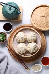 Photo of Delicious bao buns (baozi), chopsticks, sauces, seasonings and kettle on light table, flat lay