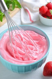 Photo of Whipping strawberry cream with balloon whisk on white wooden table, closeup