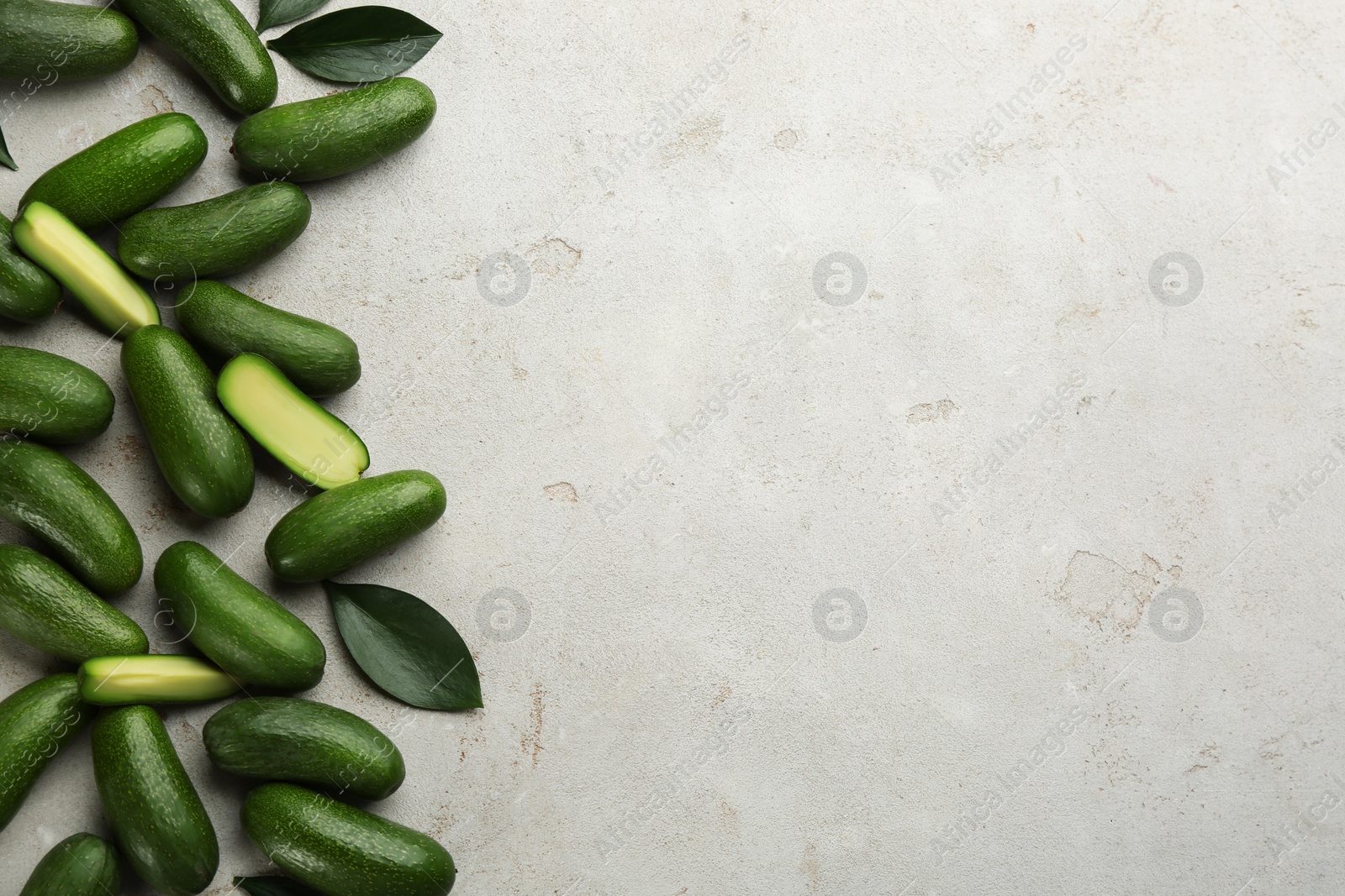 Photo of Whole and cut seedless avocados with green leaves on grey table, flat lay. Space for text