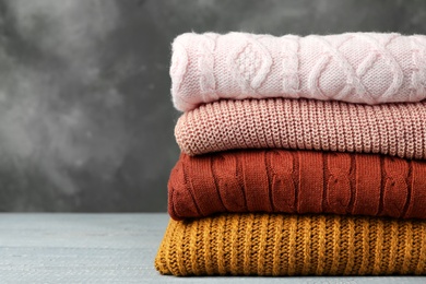 Photo of Stack of warm clothes on wooden table against grey background. Autumn season