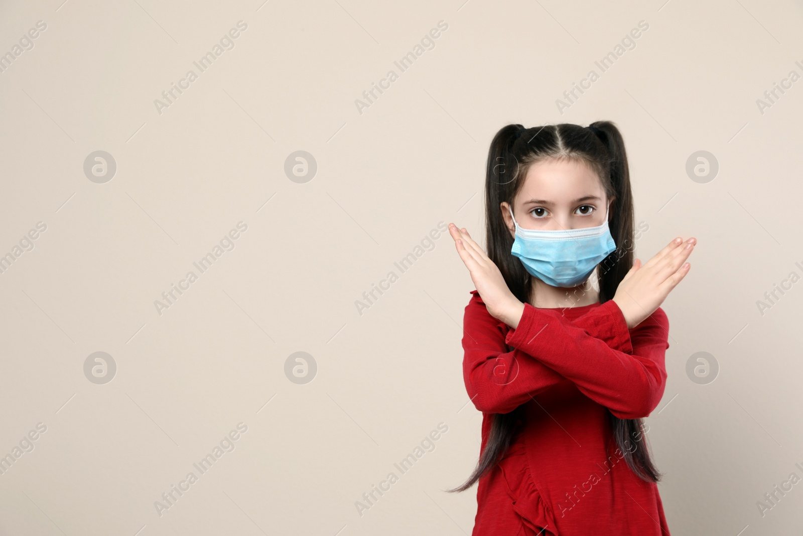 Photo of Little girl in medical mask on beige background, space for text. Virus protection