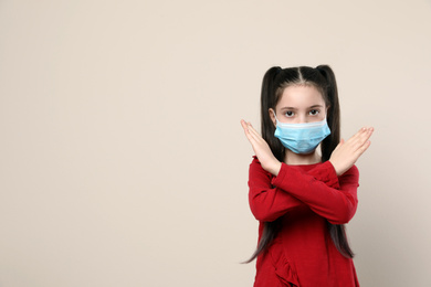 Photo of Little girl in medical mask on beige background, space for text. Virus protection