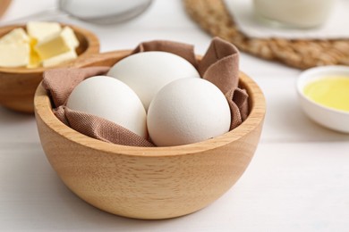 Bowl with eggs on white wooden table, closeup. Ingredients for crepes