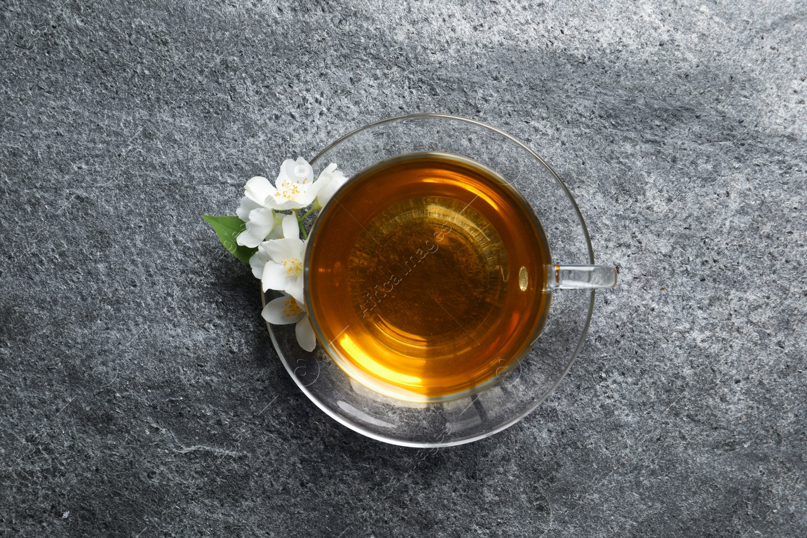 Photo of Glass cup of aromatic jasmine tea and fresh flowers on grey table, top view