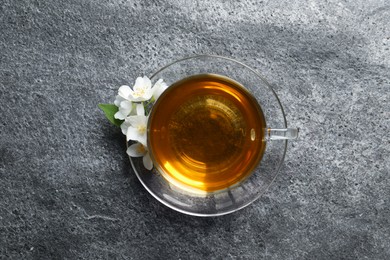 Glass cup of aromatic jasmine tea and fresh flowers on grey table, top view