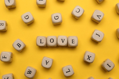 Mini cubes with letters forming word Love on yellow background, flat lay