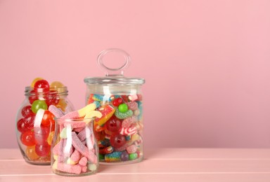 Jars with different delicious candies on pink wooden table, space for text