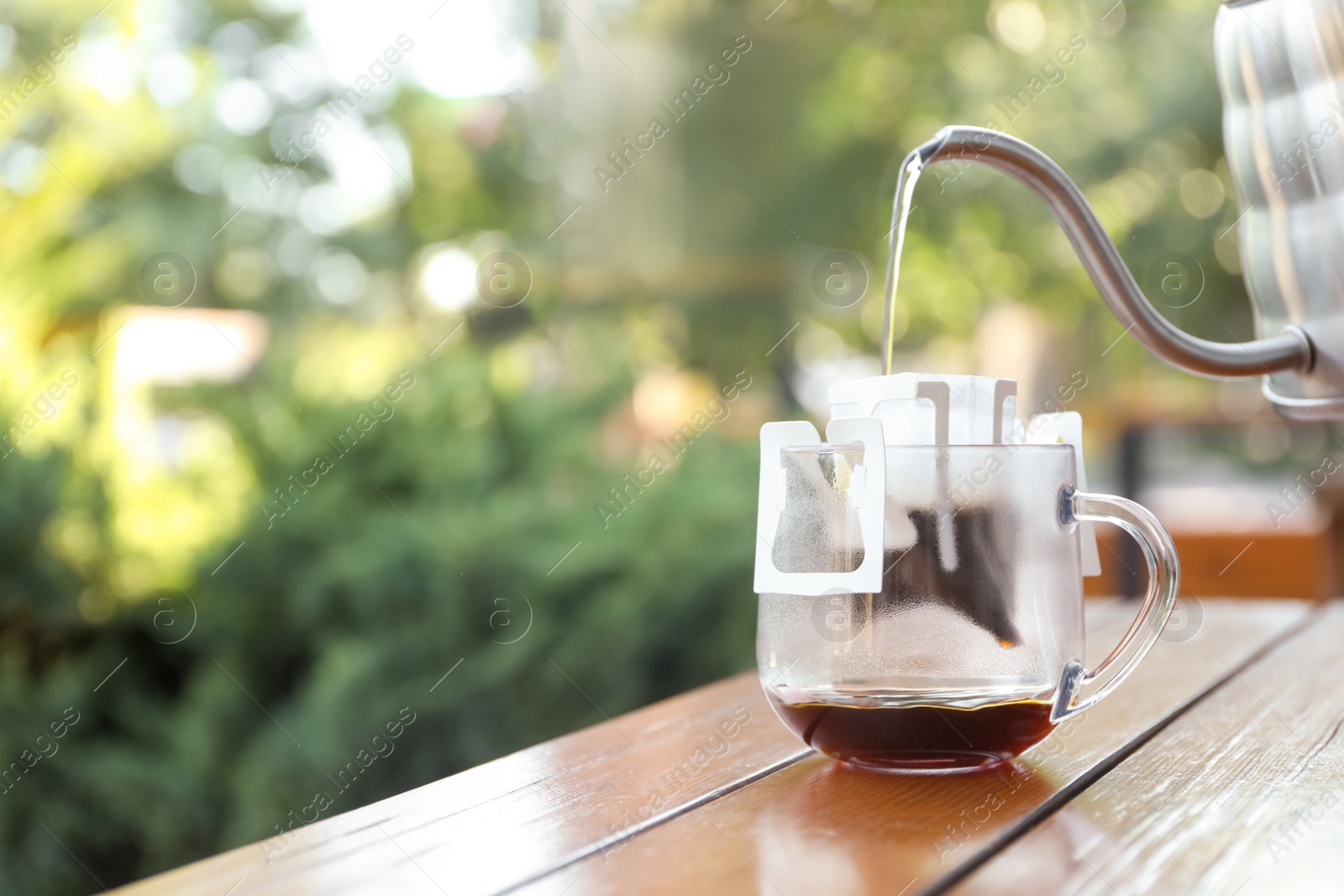 Photo of Pouring hot water into glass cup with drip coffee bag from kettle on wooden table. Space for text